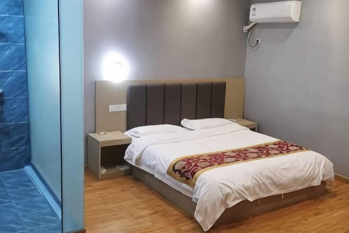 Une chambre à coucher comprenant un lit, des tables de chevet, un climatiseur fixé au mur et un espace douche.
