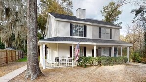 A two-story house with a porch, an American flag, and a tree with Spanish moss. - Cozy, Coastal Retreat! Minutes from Parris Island! (Port Royal)