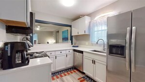 A modern kitchen with white cabinets, stainless steel appliances, a coffee maker, and a window with curtains. - Cozy, Coastal Retreat! Minutes from Parris Island! (Port Royal)