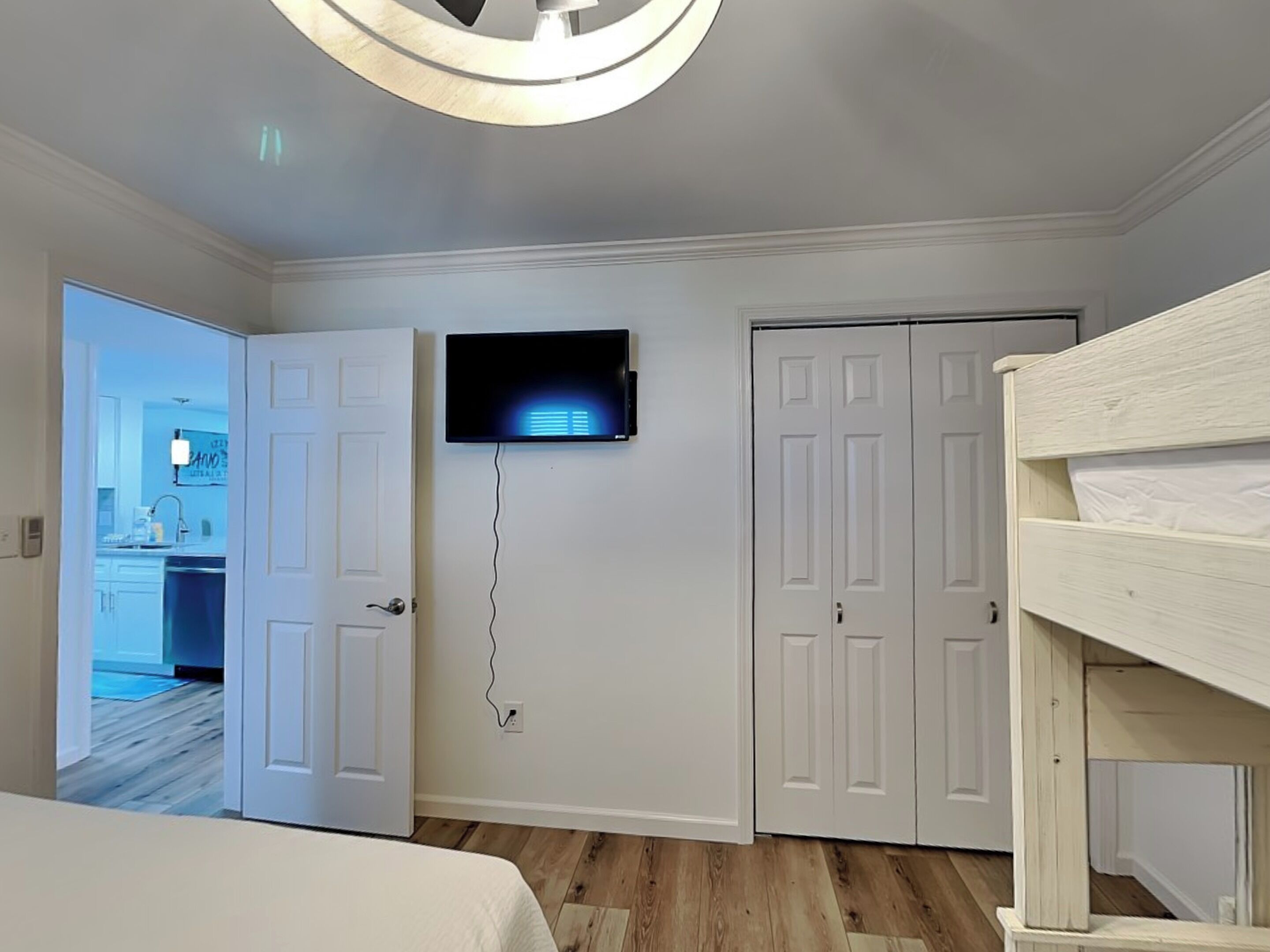Une chambre avec un lit superposé, un téléviseur fixé au mur et une porte donnant sur une salle de bain.