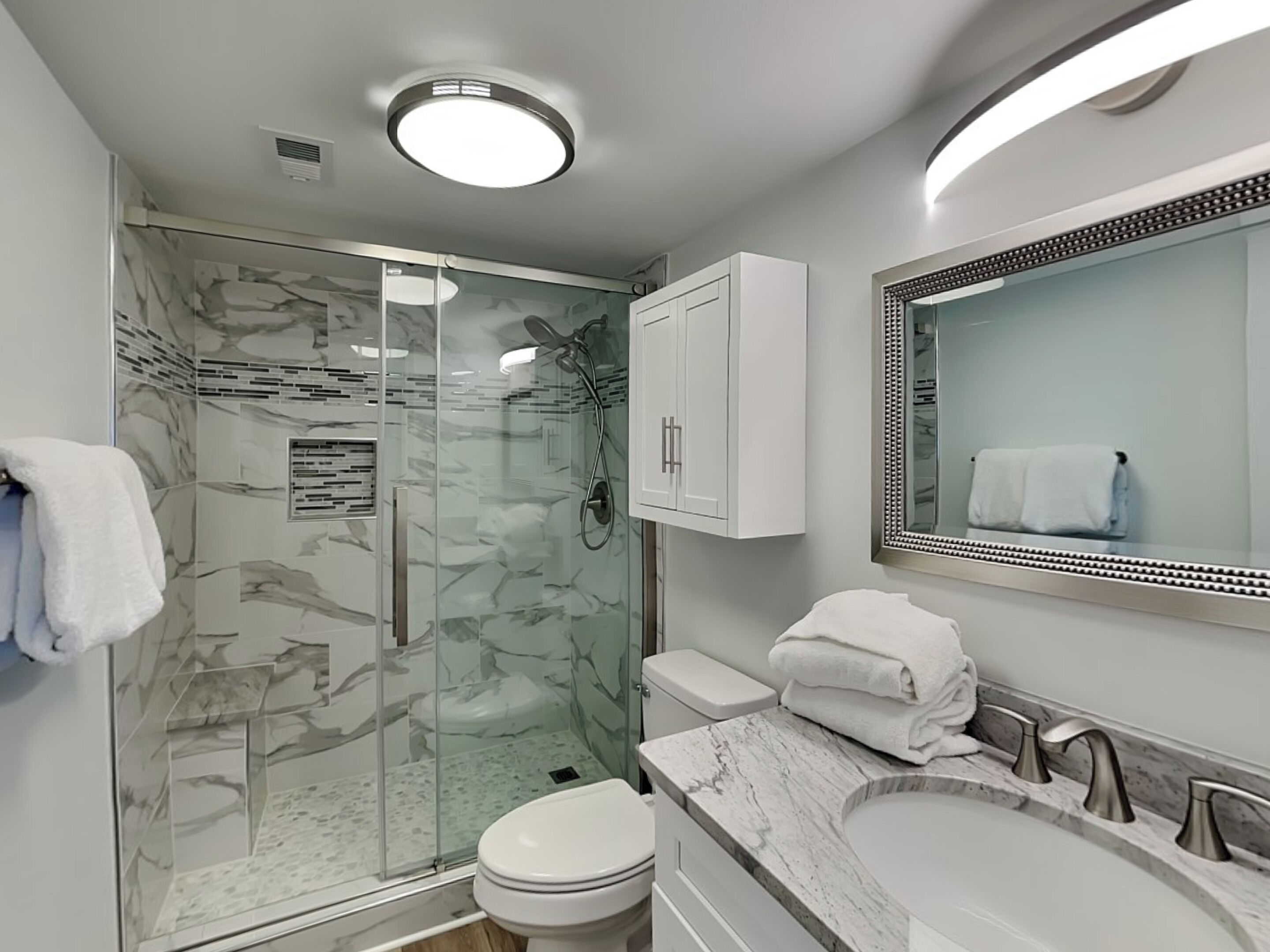 A modern bathroom with a glass-enclosed shower, a marble vanity, a large mirror, and a toilet.