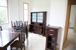 A dining area with a wooden table and chairs, a cabinet with glass doors, and a tiled floor.