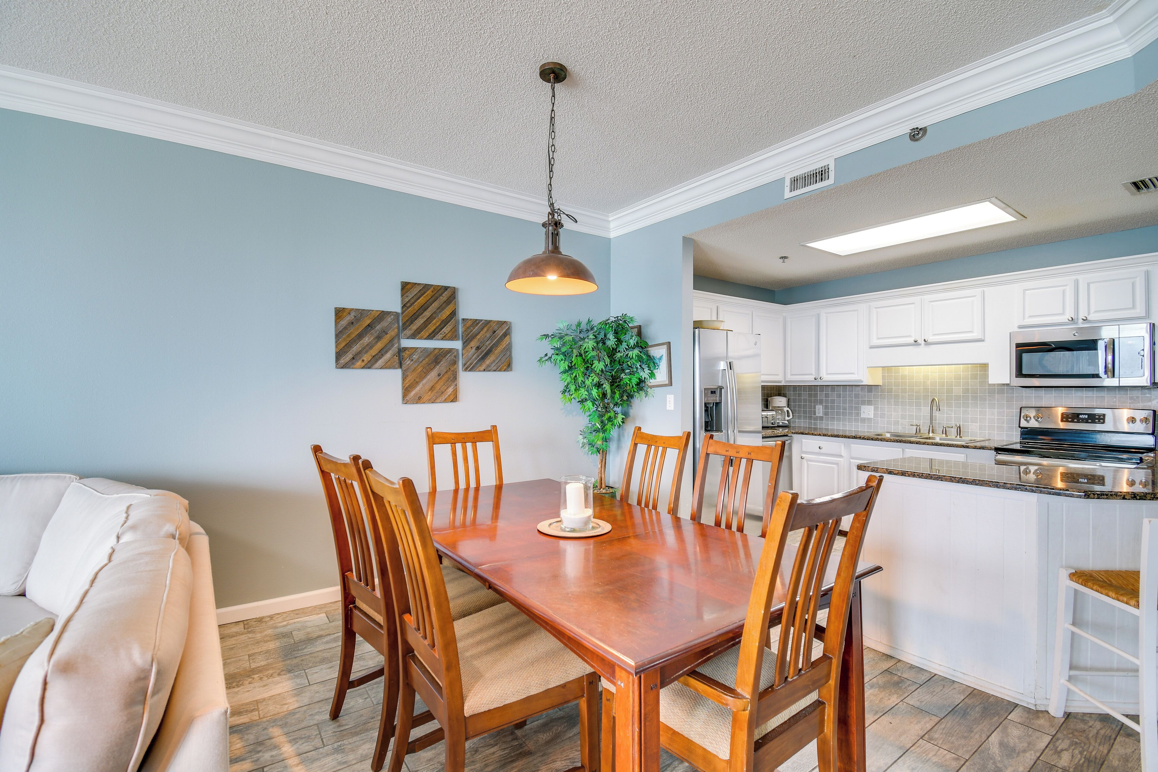 Een eethoek met een houten tafel en stoelen, een hanglamp en een keuken op de achtergrond.