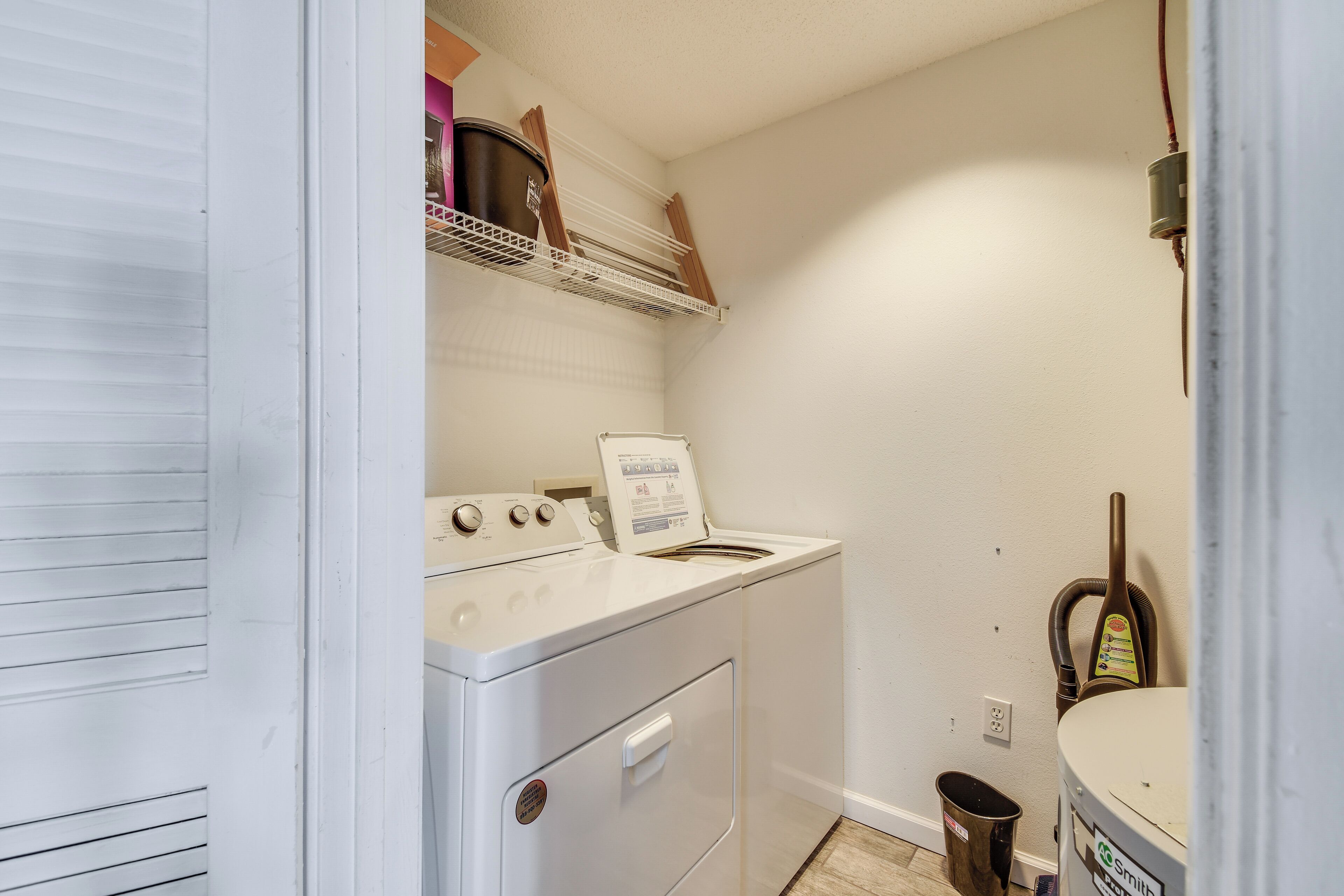 Une buanderie avec un lave-linge et un sèche-linge blancs, un balai et une poubelle.