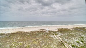 A beach with a sandy shore and a grassy area in the foreground. - Newly Renovated Oceanfront Orange Beach Condo! (Orange Beach)