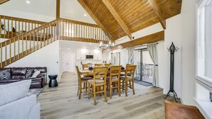 Een ruime woonkamer met een houten trap, een eettafel met stoelen, een leren bank en een groot raam.