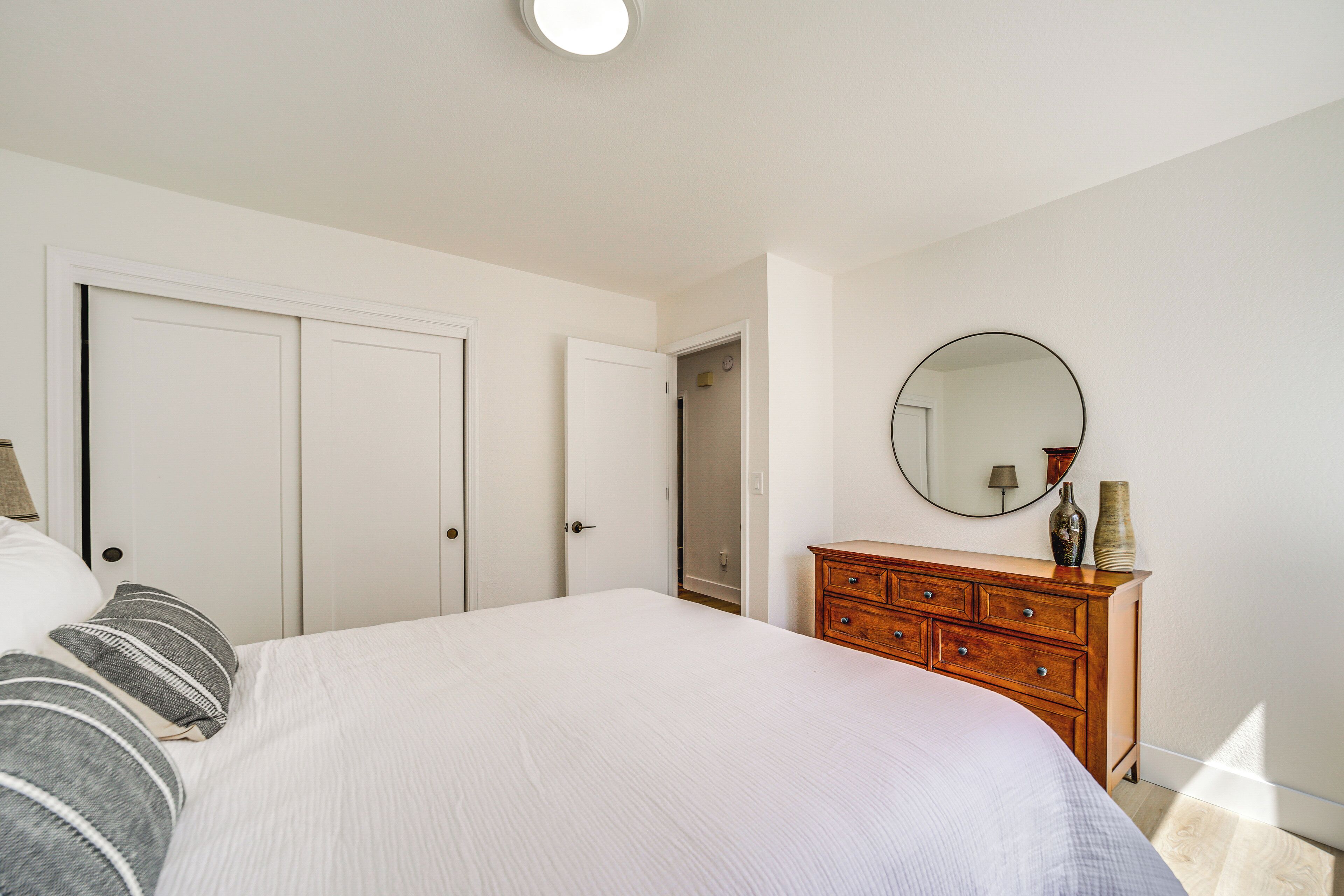 A bedroom with a large bed, wooden dresser, and a round mirror on the wall.