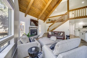 Un vaste espace de vie doté d’un haut plafond en bois, d’une cheminée, d’un escalier et d’un coin cuisine.