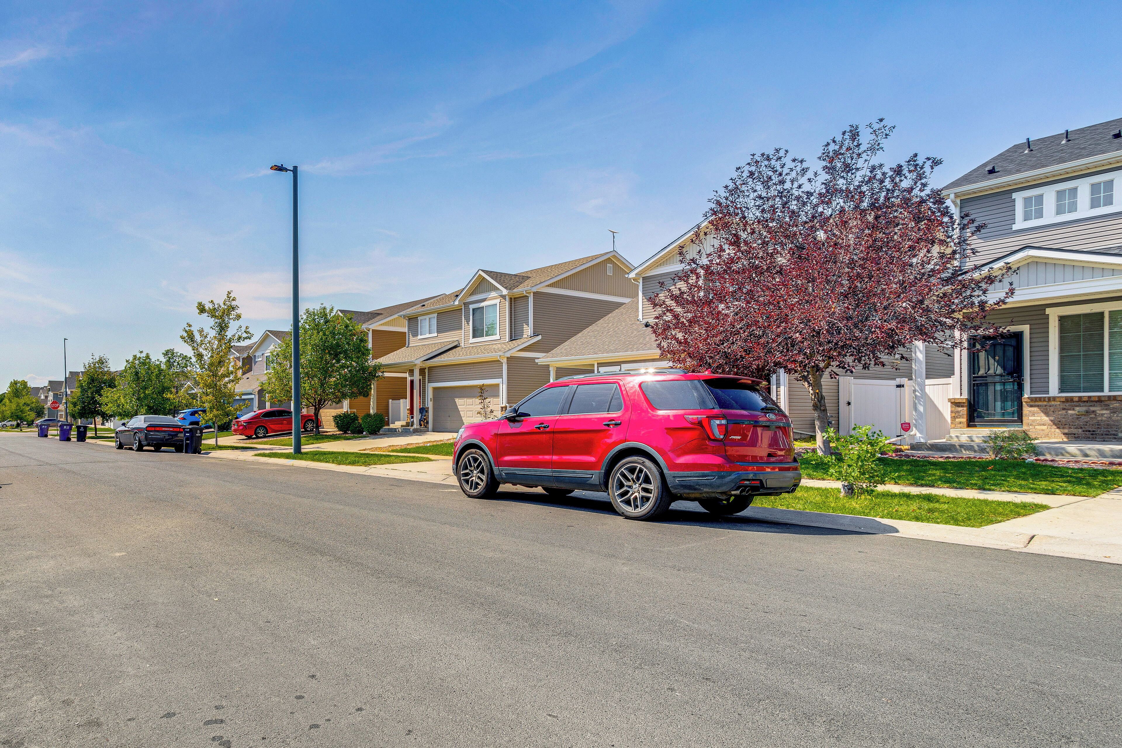 A residential street with houses, a red SUV, and a clear blue sky.