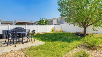A backyard with a barbecue area, a white fence, and a tree.