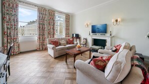A living room with a sofa, armchairs, a TV, and a fireplace. - Exceptional 2 bed, 2 bath, South Ken Apt (London)