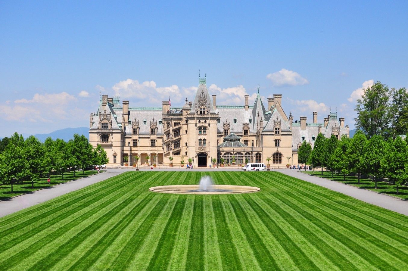 A large, historic building with a symmetrical facade, a central courtyard with a fountain, and a well-maintained lawn.