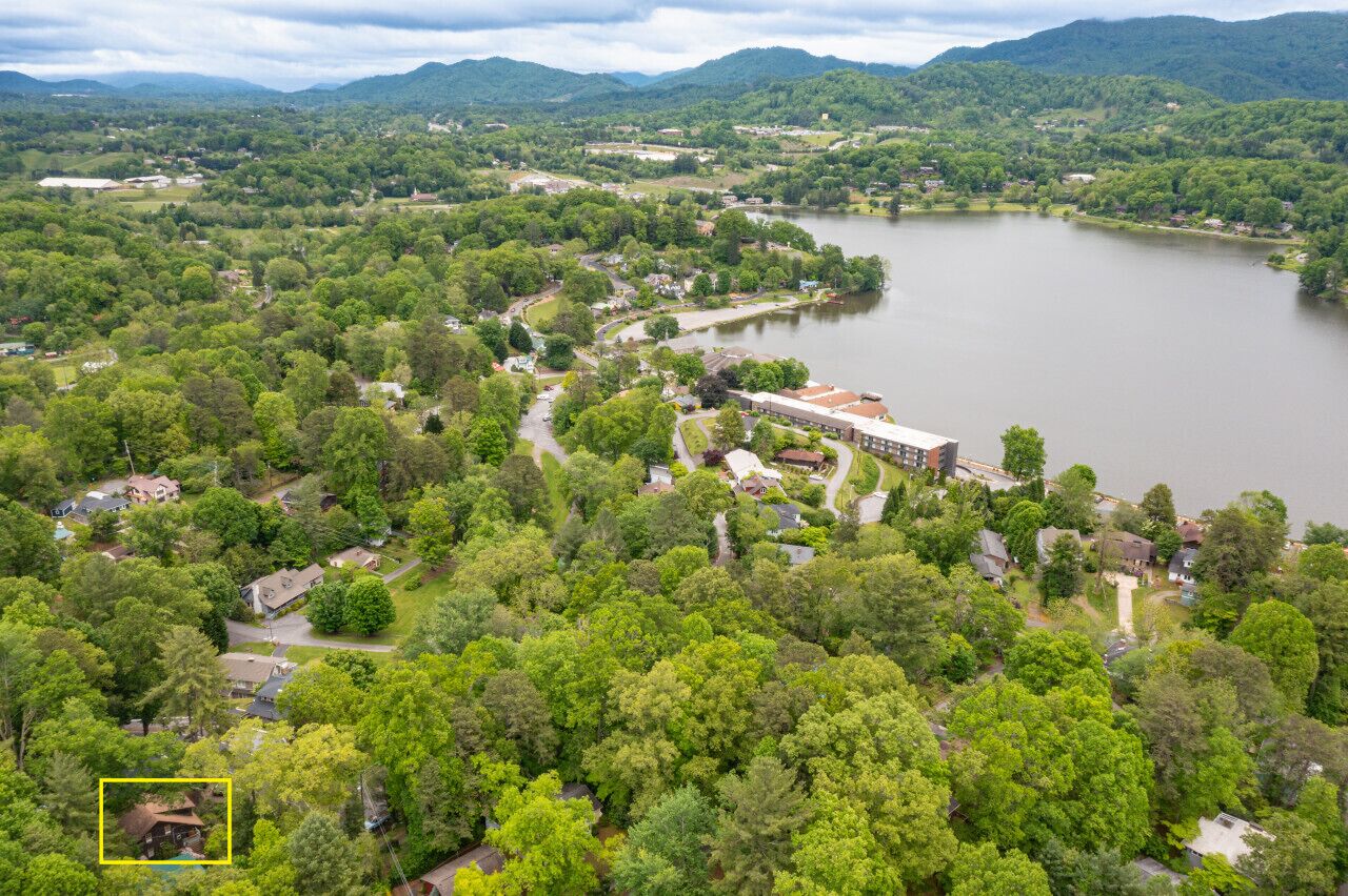 An aerial view of a residential area with a large lake, surrounded by dense greenery and hills in the background.