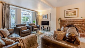 A modern living room with leather sofas, a glass coffee table, a flat-screen TV, and a brick fireplace.