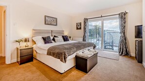 A bedroom with a bed, bedside tables, a TV, and a large window with curtains.