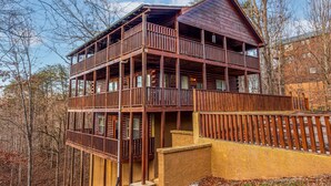 A two-story wooden cabin with a balcony, surrounded by trees.