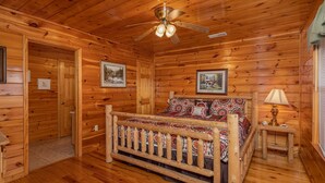 A log cabin bedroom with a wooden bed, a ceiling fan, and framed pictures on the walls.