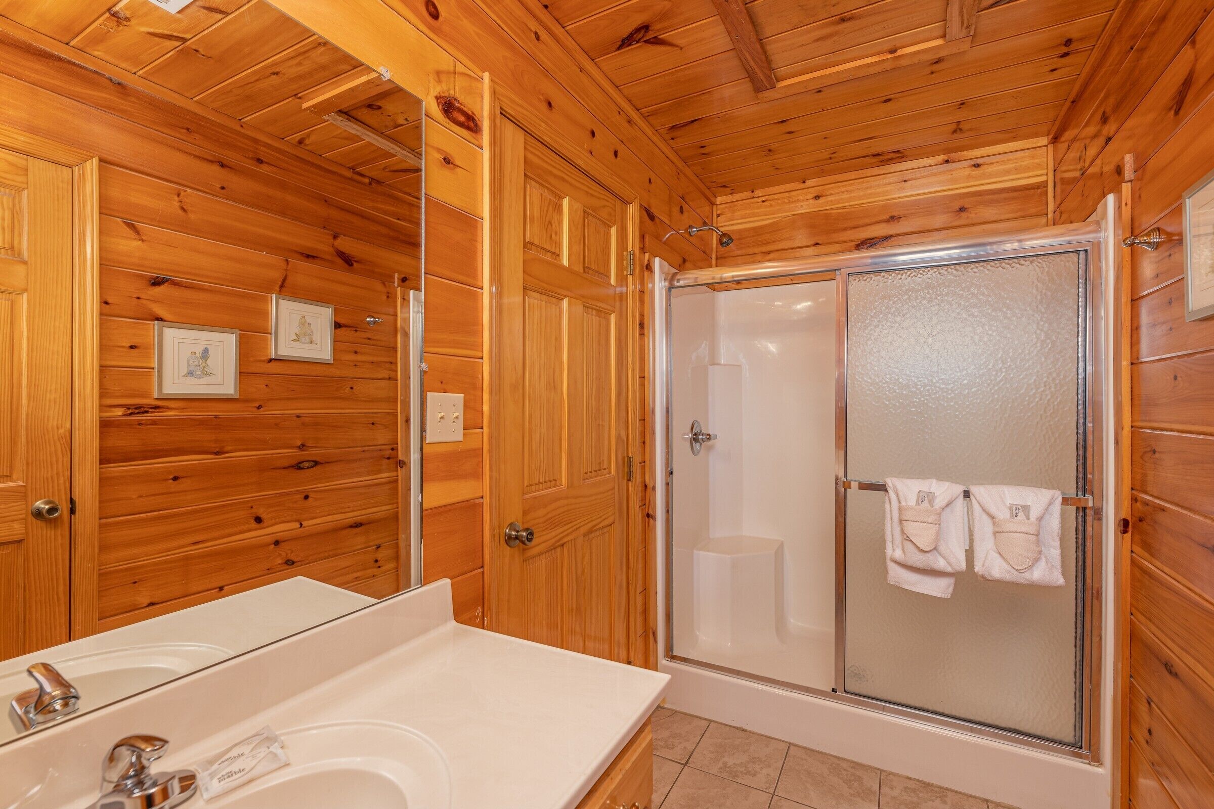 A wooden-paneled bathroom with a large mirror, a sink, and a glass-enclosed shower.