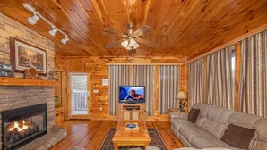 A cozy log cabin interior with a fireplace, a television, and a comfortable seating area.