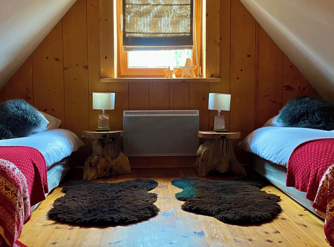 Une chambre mansardée avec deux lits, une fenêtre donnant sur un beau paysage et un radiateur.