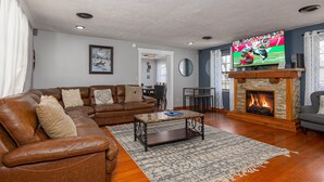 A living room with a leather sofa, a coffee table, a fireplace, and a television displaying a sports game. - Recreational Playing One On One (SEVIERVILLE)