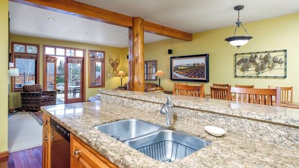 A kitchen with granite countertops, stainless steel sinks, wooden cabinets, and a dining area with wooden chairs. - Charming 2-bedroom condo! (Rossland)