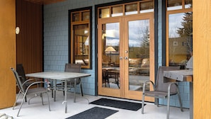A patio area with a table and chairs, a wooden door with glass panels, and a view of the outdoors. - Charming 2-bedroom condo! (Rossland)