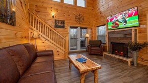L’intérieur chaleureux d’un chalet, avec un décor en bois, une cheminée, un téléviseur et un canapé en cuir.