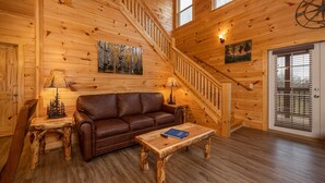 L'intérieur d'un chalet en bois, avec un escalier, un canapé en cuir marron, une table basse en bois et un tableau accroché au mur.