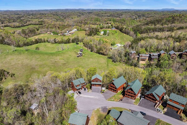 A lodge with multiple log cabins, a central building, and a large parking area surrounded by forested hills. - Private Pool Party Bliss (PIGEON FORGE)
