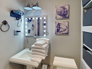 A bathroom with a sink, mirror with lights, two wall-mounted lights, and two artwork pieces.