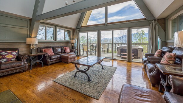 A spacious living room with leather sofas, a wooden coffee table, and large windows offering a view of the outdoors. - Your Family Reunion Getaway (GATLINBURG)
