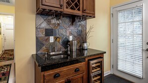 Una cocina con armarios de madera, encimera de granito, refrigerador para vino empotrado y una ventana con persianas.