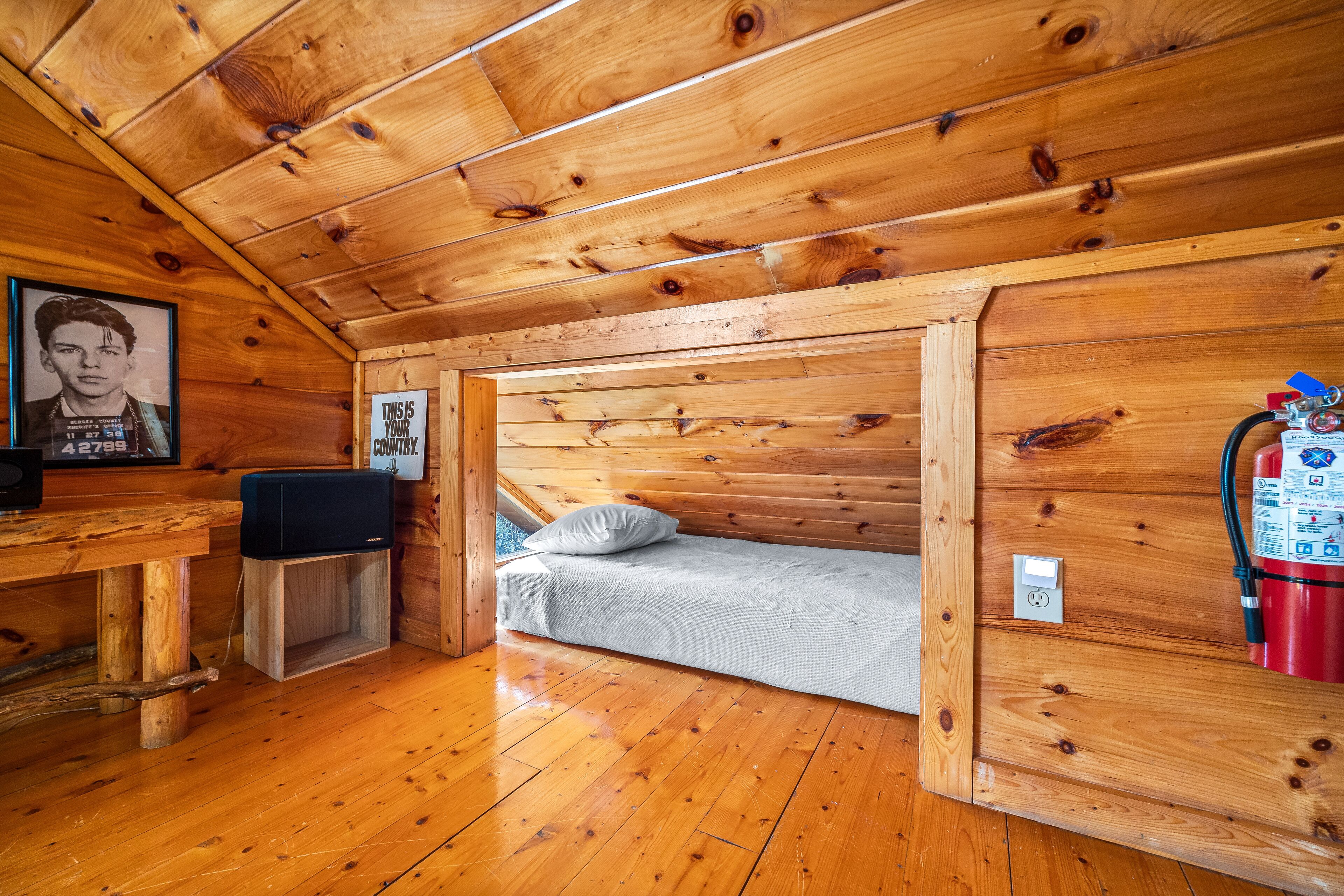 Habitación de cabaña de madera con cama, escritorio, silla, televisor y extintor.