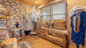 A cozy room with a stone wall, wooden furniture, a large window with blinds, and a blue garment hanging on the wall. - Luxury Mountain View Cabin with Panoramic Smoky Mountain Views (SEVIERVILLE)