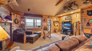 A cozy log cabin interior with a fireplace, leather furniture, and rustic decor. - Luxury Mountain View Cabin with Panoramic Smoky Mountain Views (SEVIERVILLE)