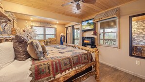 A cozy bedroom with a wooden bed, a fireplace, and a stone wall. - Luxury Mountain View Cabin with Panoramic Smoky Mountain Views (SEVIERVILLE)