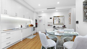 A modern kitchen with white cabinets, a glass dining table, and a white chair.