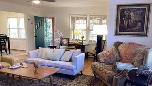 Un salon avec un canapé, des fauteuils, une table basse et un tableau accroché au mur.