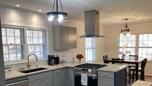 Une cuisine moderne avec des meubles gris, un four encastré, un évier et un coin repas comprenant une table et des chaises.