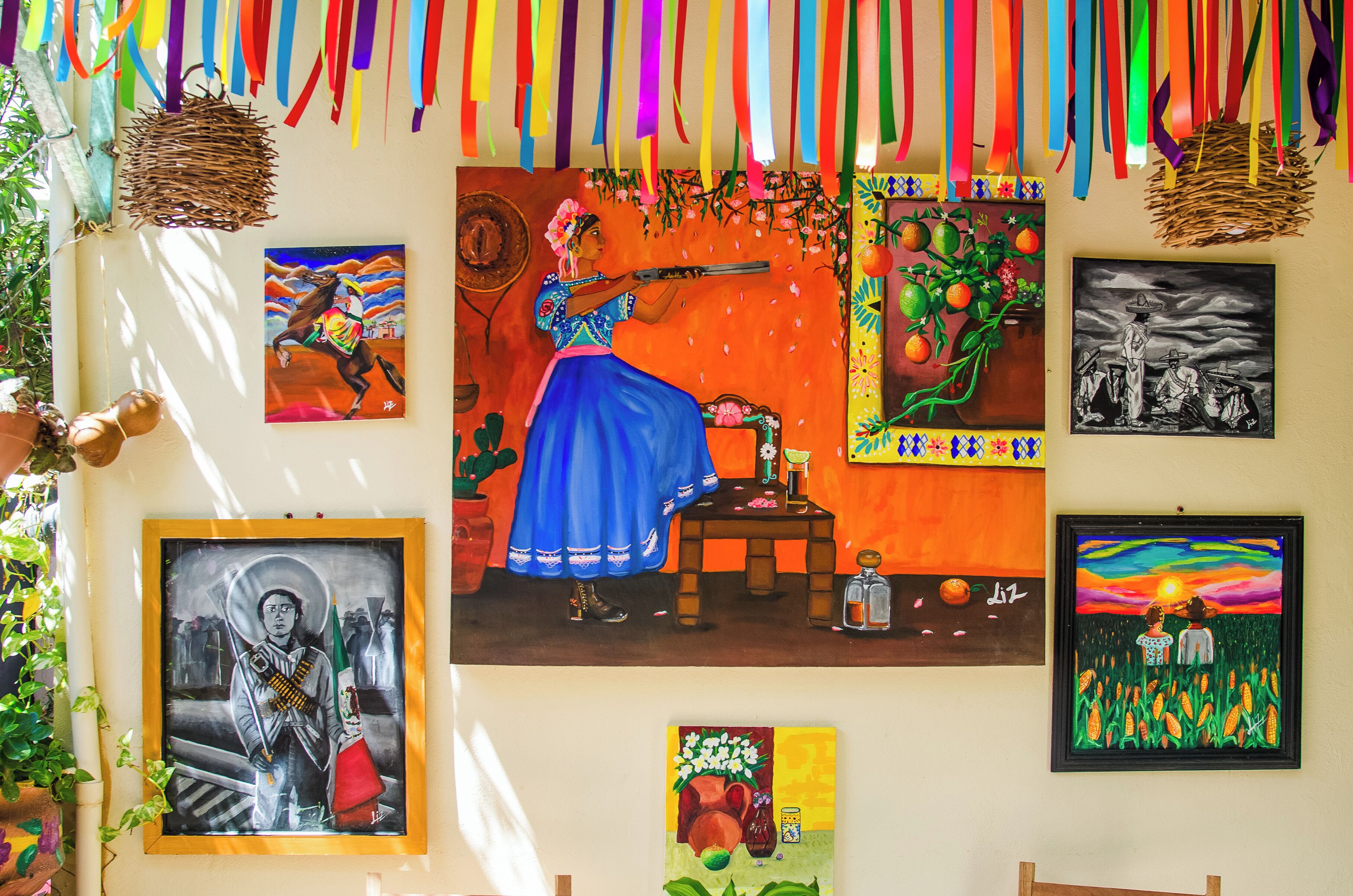 Eine Wand mit verschiedenen gerahmten Kunstwerken, darunter Gemälde und Fotografien, sowie einer farbenfrohen Wanddekoration.