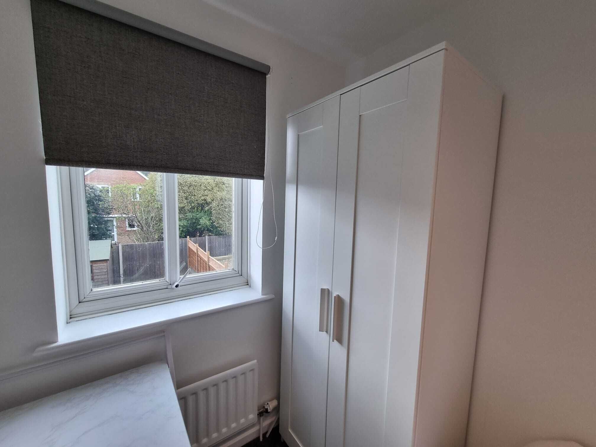 A room with a window, a radiator, and a white wardrobe.