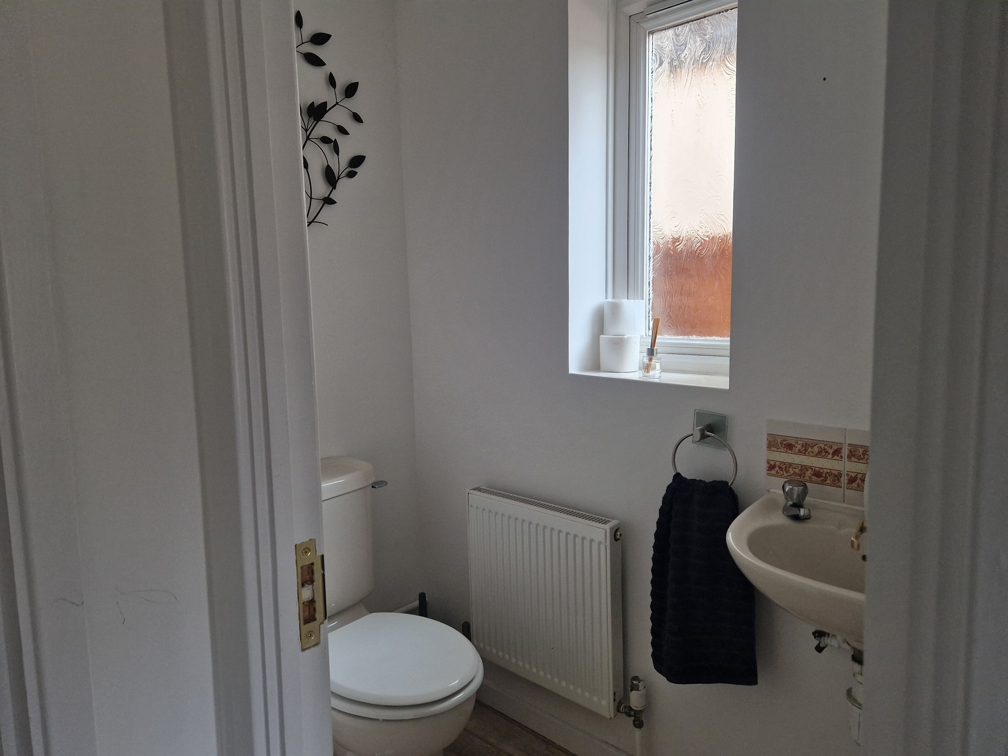Ein kleines, weißes Badezimmer mit Toilette, Heizkörper, Waschbecken und Fenster.
