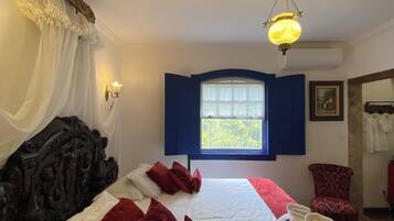 Una habitación de hotel con una cama grande, una ventana con contraventanas azules, un candelabro y una silla roja.