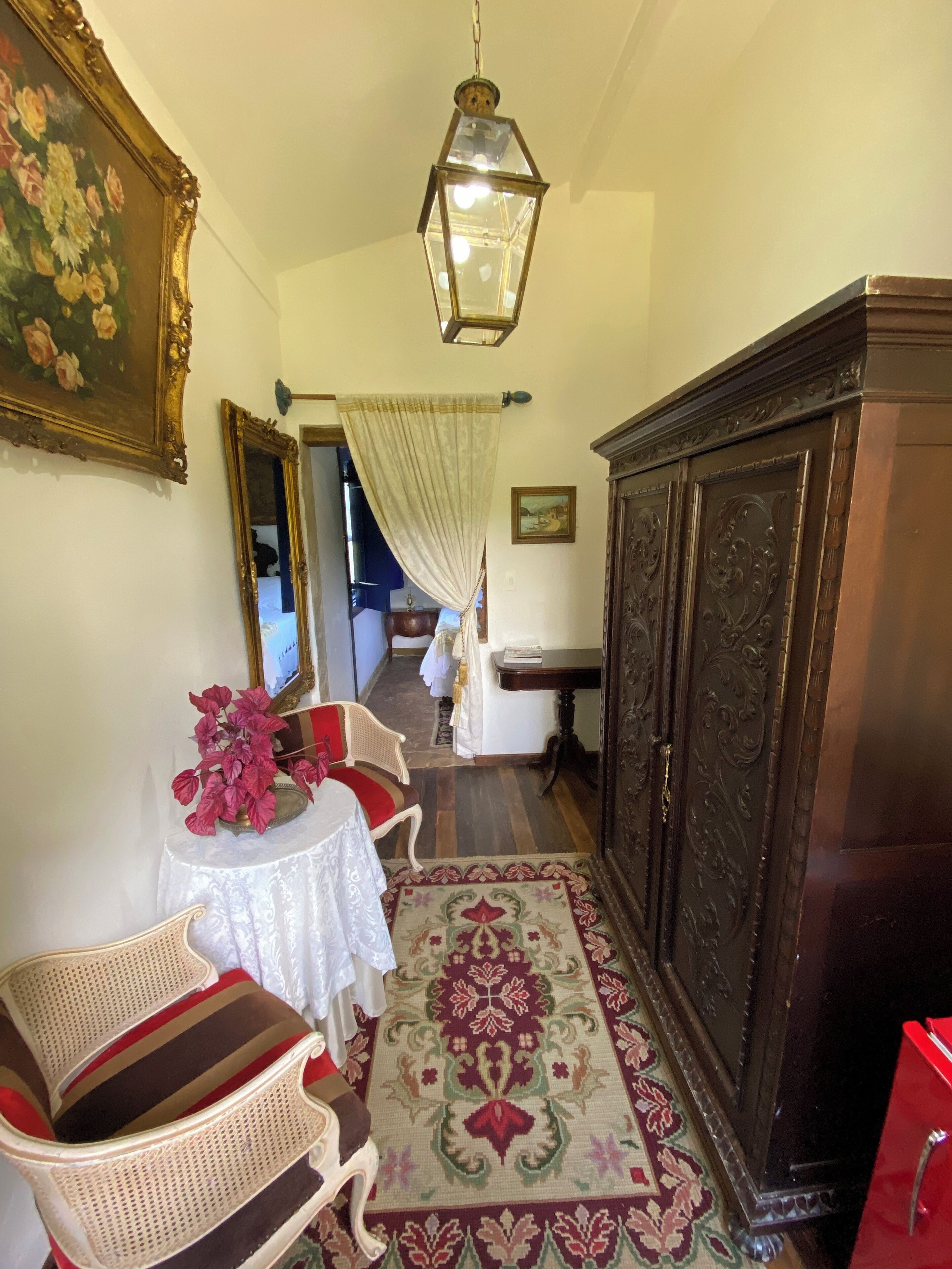 A hallway with a wooden cabinet, a wicker chair, a table with a vase of flowers, and a patterned rug.