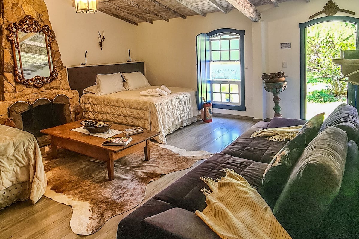 A rustic room with a bed, a sofa, a wooden table, and a stone wall.