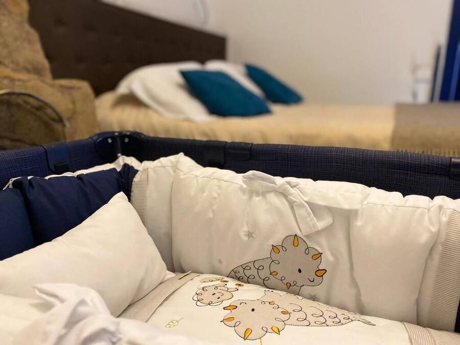 Ein Schlafzimmer mit einem Bett im Hintergrund, einem blauen Sofa mit weißen Kissen und einem weißen Kopfkissen mit Blätermotiv.