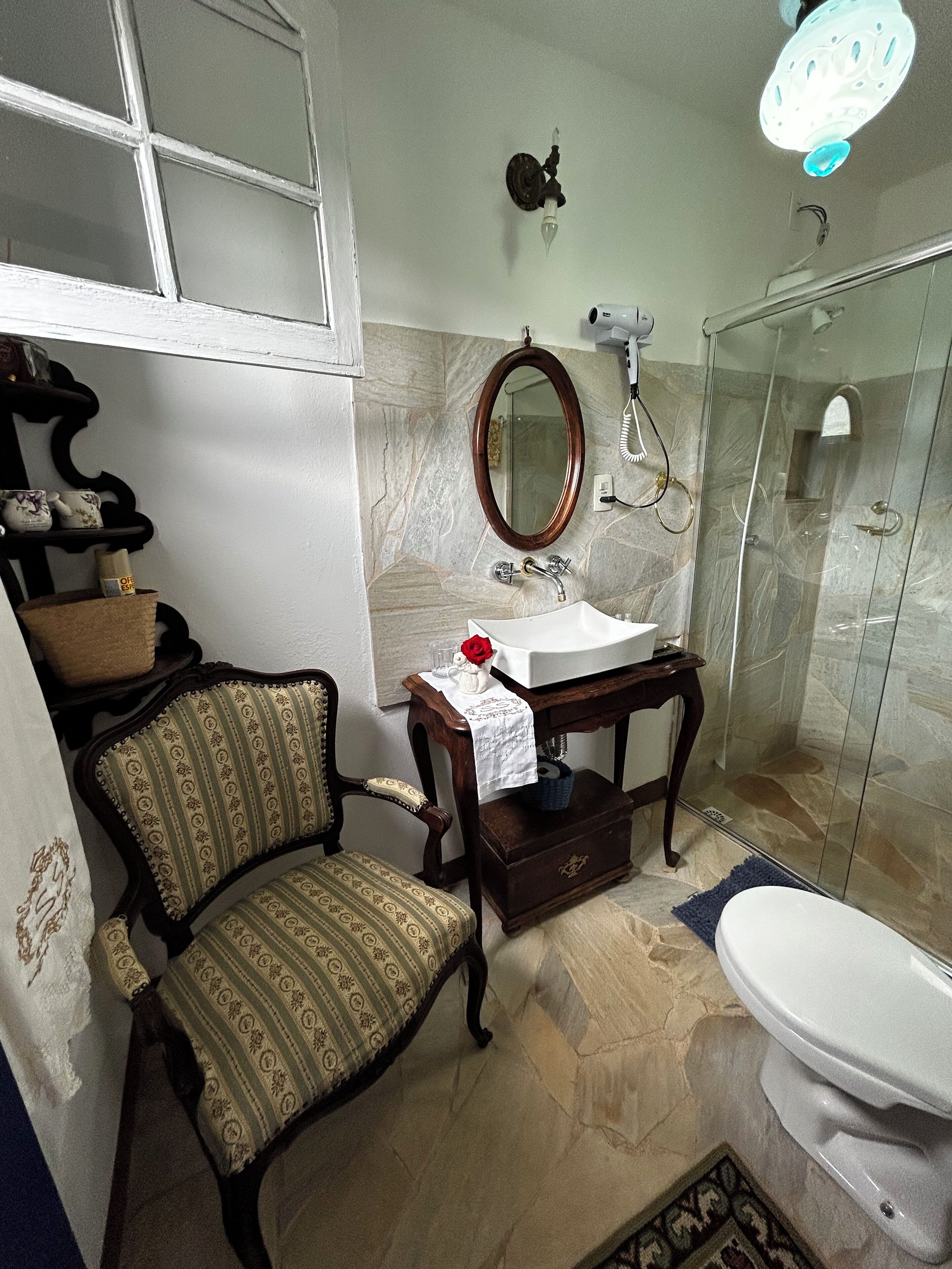 Une salle de bain avec un lavabo en marbre, une chaise en bois, un miroir et une cabine de douche en verre.