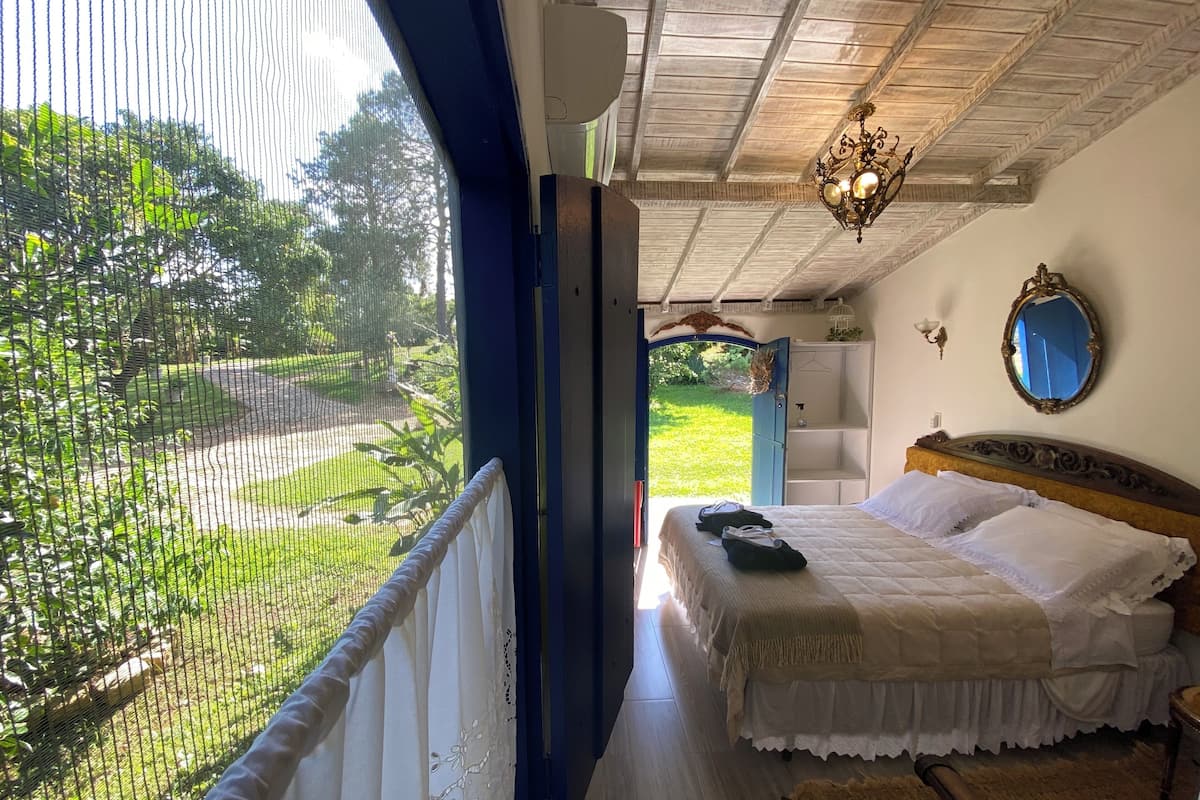 A bedroom with a bed, a mirror, and a view of a garden through a window.