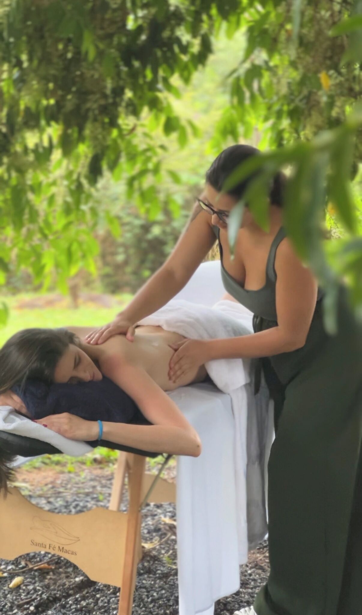 Uma pessoa recebendo massagem ao ar livre, com uma mesa de massagem e uma toalha.